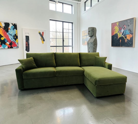 Green Comfy 18 Lux sectional sofa bed in a room with abstract art on the walls.