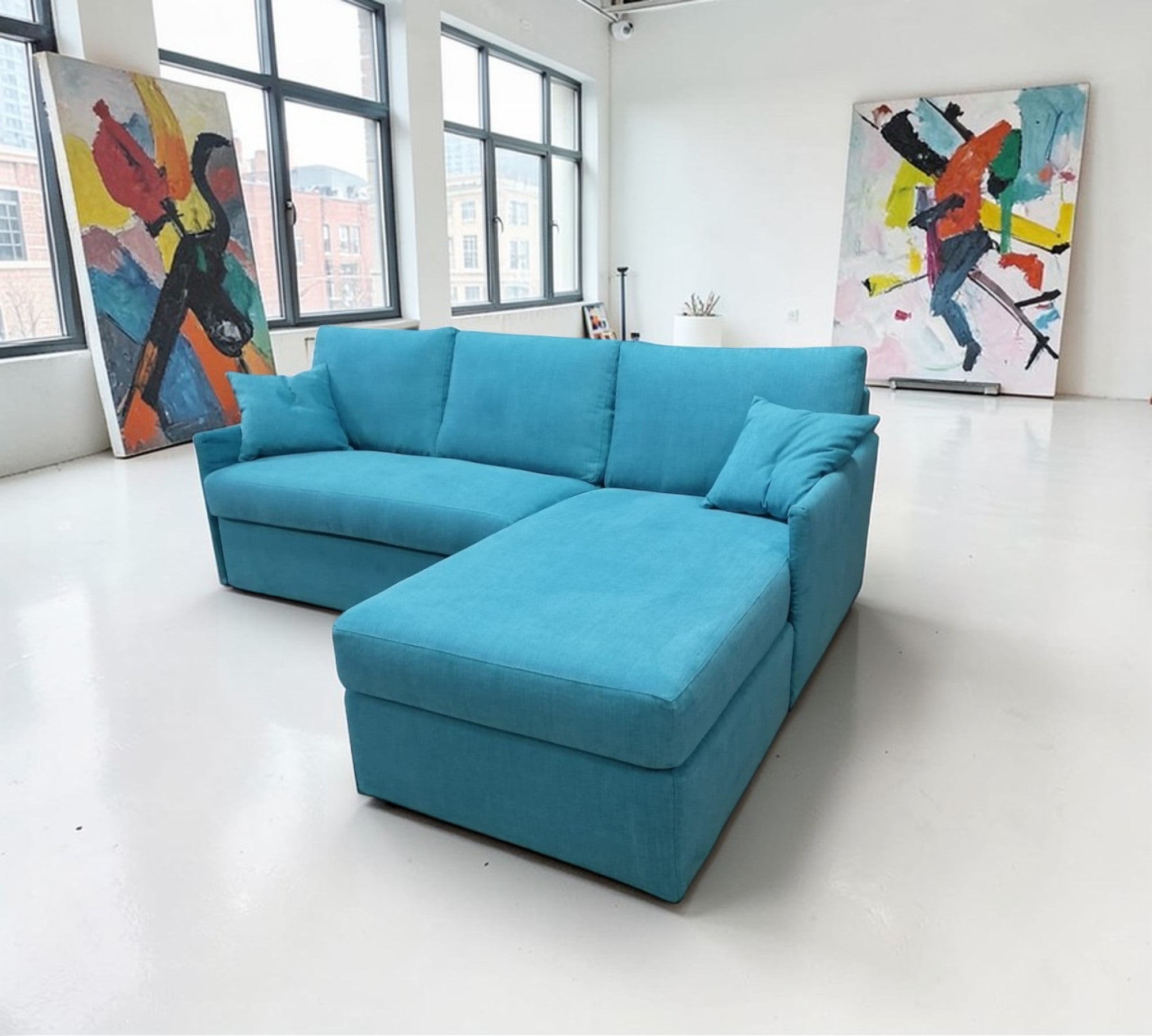 Blue Comfy 14 sectional sofa  in a room with large windows and colorful abstract paintings on the walls.