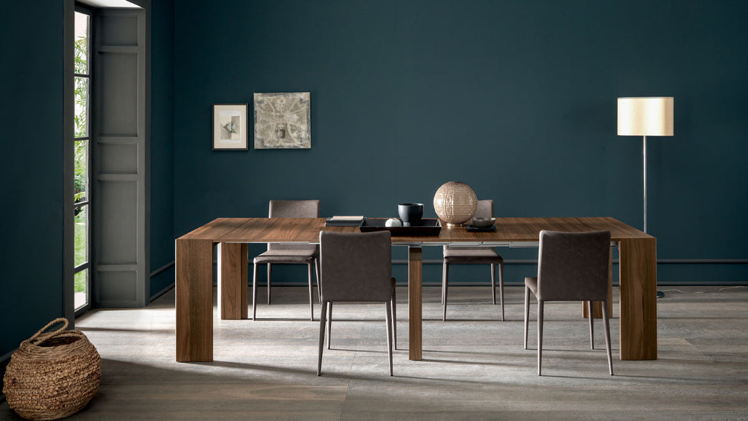 Goliath modern dining room with wooden table and chairs against a dark blue wall.