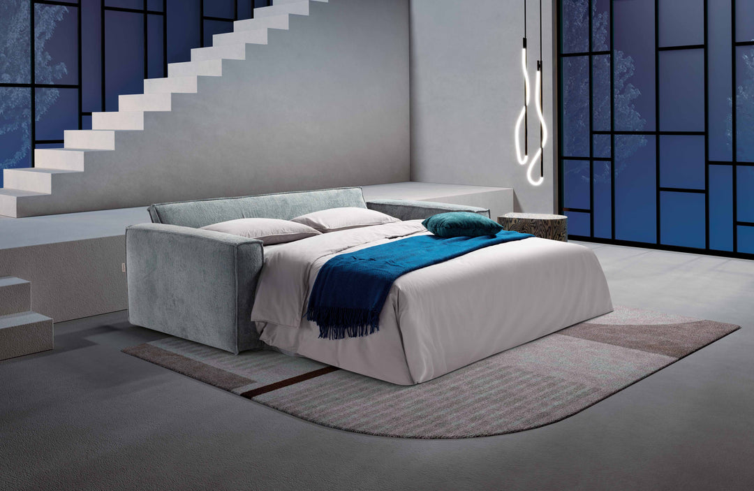 Modern bedroom with a Lush sofa bed, blue blanket, and staircase in the background.