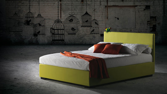 Malibu storage bed with white bedding and red pillows in a dimly lit room with brick walls and hanging birdcages.