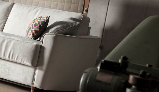 Grey Petrucciani sofa or sofa bed with a colorful pillow and a camera on a tripod in the foreground.