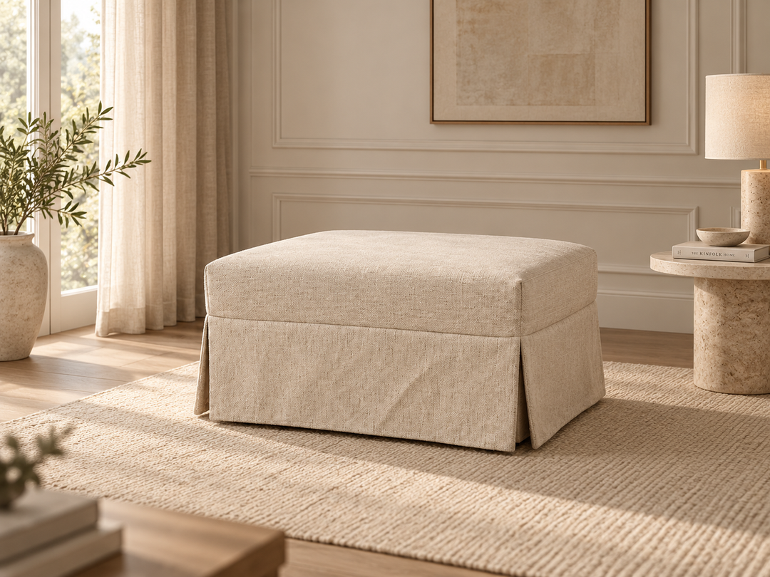 Pop our square upholstered ottoman bed in a light beige fabric, styled in a bright, modern room with a matching rug, side table, and lamp.
