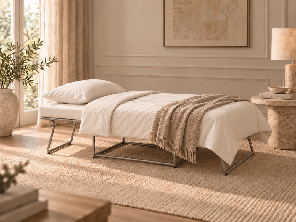 Pop modern ottoman bed with a white upholstered seat and backrest, supported by slim black metal legs, styled with white bedding and a beige fringed throw blanket in a warm, sunlit bedroom.